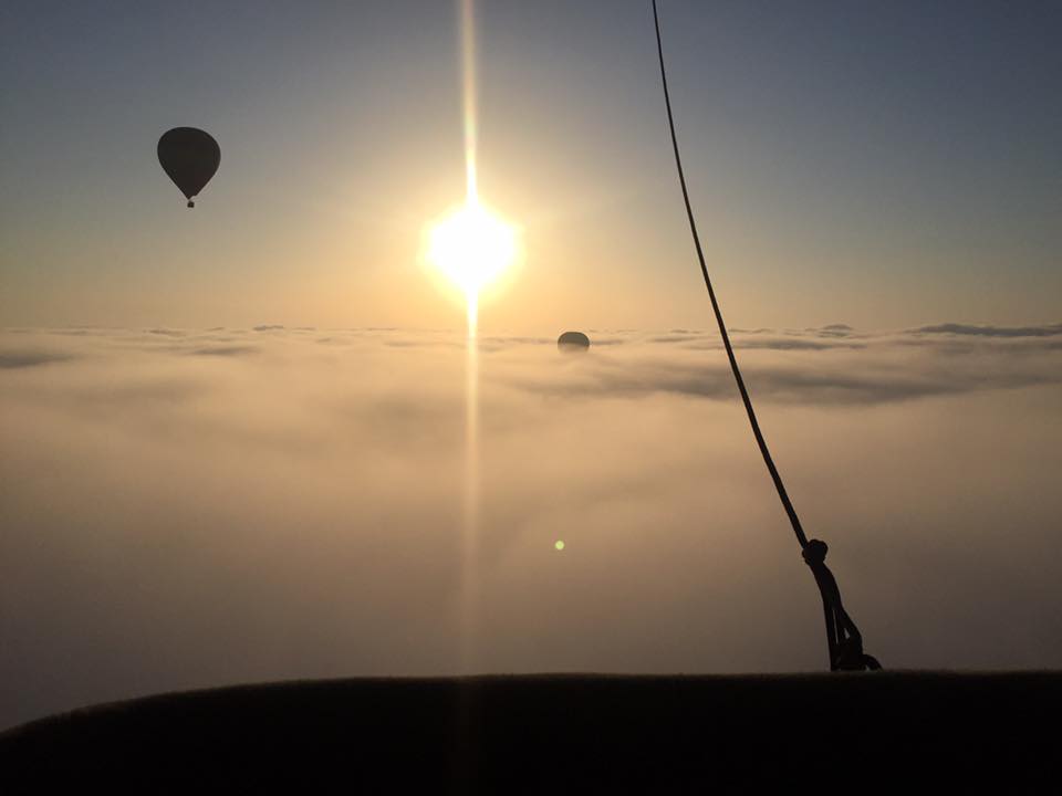 Plusieurs montgolfieres volent au dessus des nuages avec un magnifique soleil.